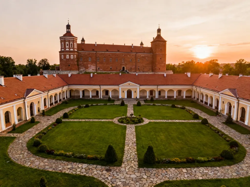 Widok na odrestaurowany Zamek Janów Podlaski w świetle zachodzącego słońca, otoczony zadbanym dziedzińcem.